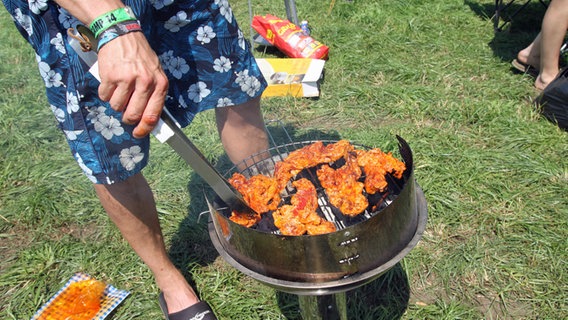 Ein Festivalbesucher beim Deichbrand 2014 wendet das Fleisch auf einem Grill. © NDR Foto: Anthrin Warnking