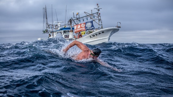 Extremschwimmer André Wiersig schwimmt im Meer - hinter ihm fährt ein Begleitboot. © Dennis Daletzki Foto: Dennis Daletzki