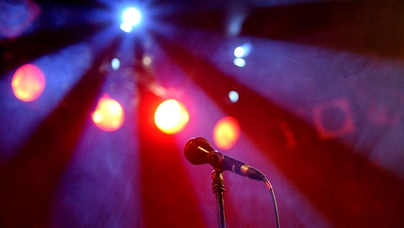 Ein Mikrofon auf einem Ständer, im Hintergrund rote und blaue Bühnenbeleuchtung. © Picture Alliance Foto: Britta Pedersen